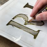 Tracing letters of a stencil with a pyrography marker on a wood halloween tombstone - How To Holiday