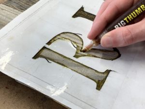 Tracing letters of a stencil with a pyrography marker on a wood halloween tombstone - How To Holiday