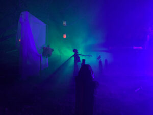 Halloween 2020 - Halloween corpse in graveyard cemetery under green and purple lighting with halloween candles and fog machine fog